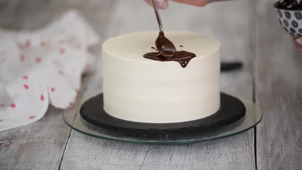 Closeup of a Pastry Chef Pouring Liquid Chocolate on a White Cream Cake