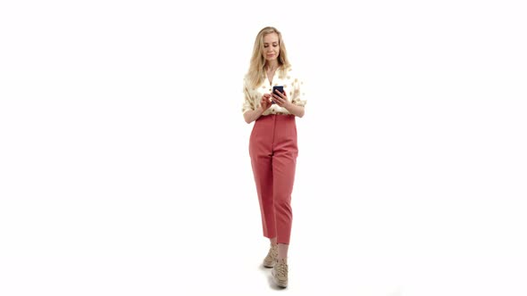Nice Caucasian Blonde Girl Looking Into the Phone Wearing Shirt and Pink Trousers Full Shot White alt