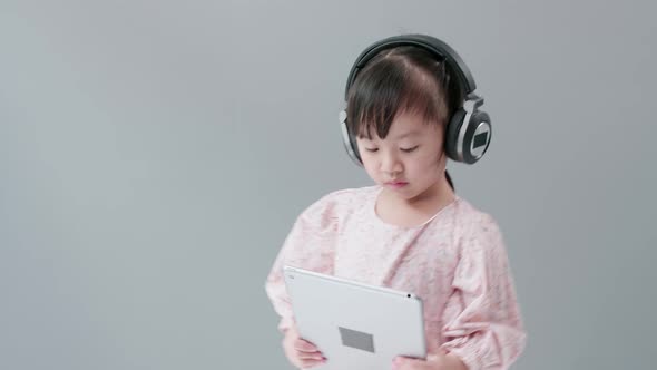Little Asian girl with headphone enjoy watching video online on tablet and dancing happily. alt