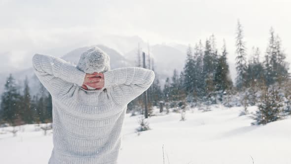 Young Woman in White Sweater and Woolen Hat Enjoying Mountain Landscape and Snowfall alt