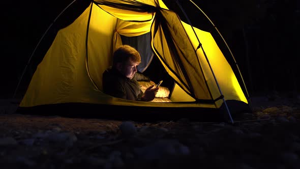 The Traveler Lay Down to Watch the News on His Smartphone in a Yellow Tent