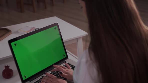 Home Isolated. Woman at Home Sitting on a Couch Works on a Laptop Computer with Green Mock-up Screen