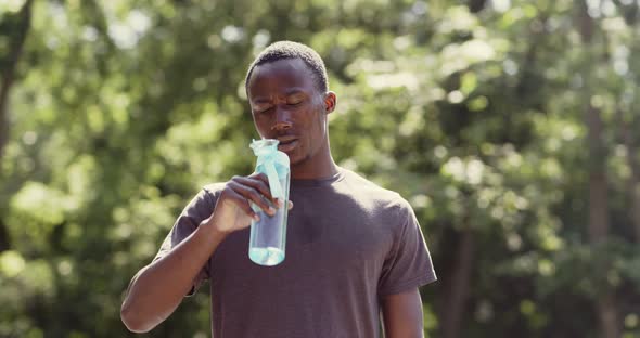 Overheated African American Guy Drinking Water From Bottle in Park alt