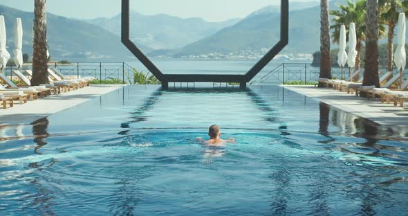 Back view of active man in the swimming in pool in hotel resort during the vacation alt