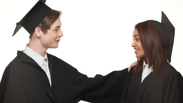 Caucasian Happy Graduate Young Male Giving High Five to Smiling African American Female in Black alt
