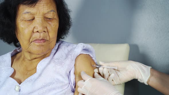 Doctor giving vaccine injection into senior woman shoulder