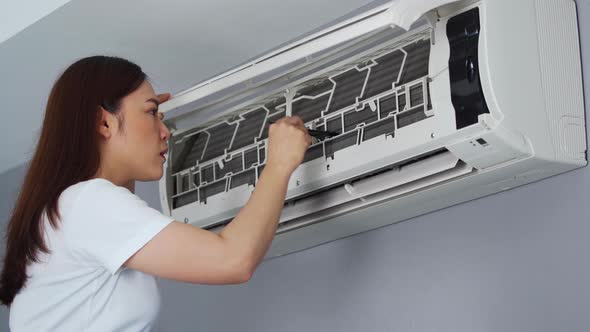 young woman using brush to cleaning the air conditioner indoors at home