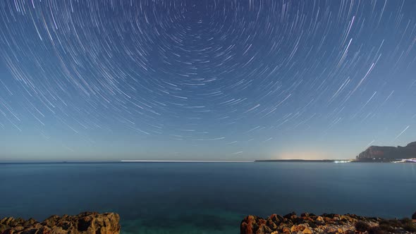 Startrails around polaris over rocky coastline of mediterranean sea with clear turquoise water at na alt