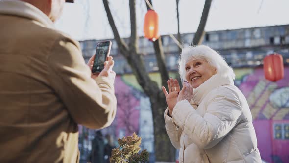 Elderly Couple Takes Photos Smiling on a Smartphone on a Modern Street
