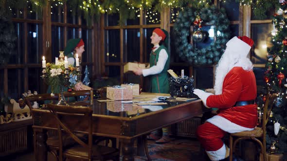 Santa Claus is Writing a Letter on the Typewriter and Watching Elves  alt