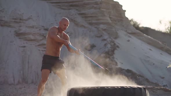 Bald Man Strongman Hits a Hammer on a Huge Wheel in the Sandy Mountains in Slow Motion. Strength and alt