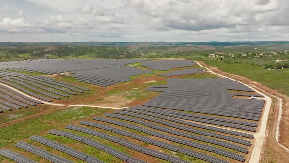Long aerial shot of a medium-sized solar farm built on hills in the Portuguese countryside, next to alt