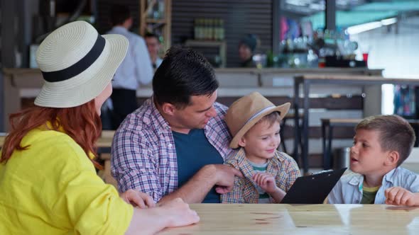 Joyful Happy Family of Parents with Children Have Fun at Table in Cafe and Choose Food and Drinks