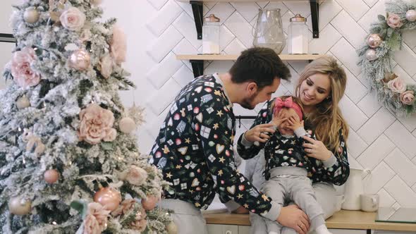 A Young Family in Warm Sweaters with a Baby Daughter in a Christmas Bedroom alt