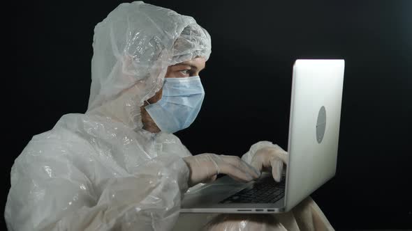 Scientist Man in a Protective Suit and Mask Typing on a Laptop Night Writes Patient Reports in alt