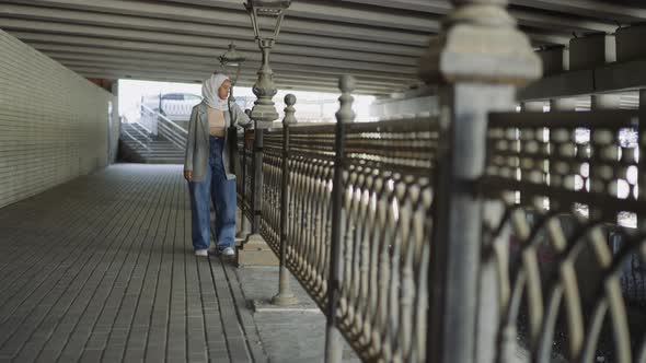 Black Muslim Woman Rests Near Handrail on City Embankment alt
