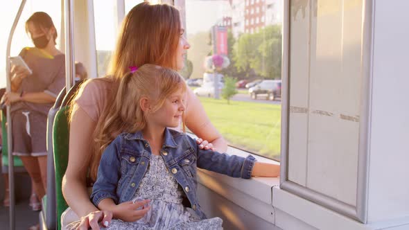 Family Rides in Public Transport Woman with Little Child Girl Sit Together and Look Out Window Tram alt
