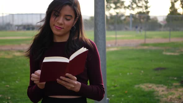 A young woman university student reading a textbook outdoors in the campus park at sunset SLOW MOTIO alt