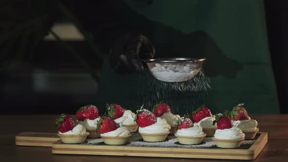 Chef sprinkling sugar powder on tasty mini cake with cream and strawberries alt
