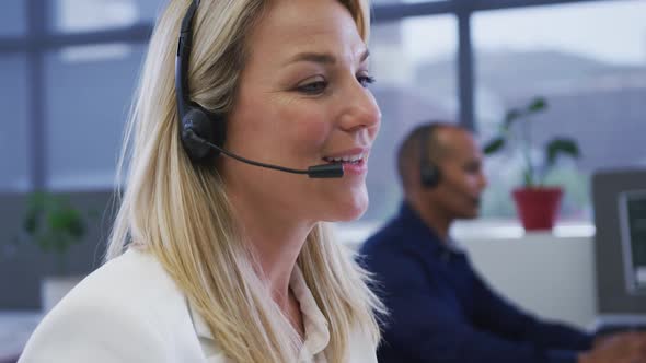 Diverse business people sitting using computers talking with phone headsets alt