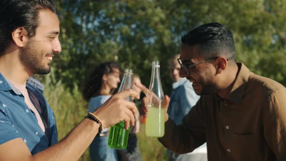 Happy Middle Eastern Men Clinking Bottles with Drinks and Talking Outdoors at Beach Party alt