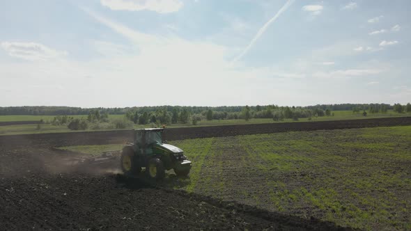 Agricultural green big tractor plows in the field. alt