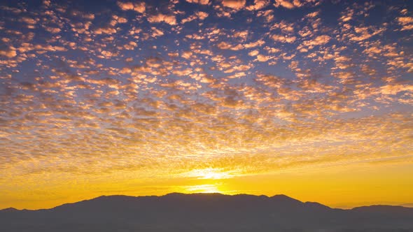 Aerial view of morning orange gold sky cloudscape over fertile forest mountains.