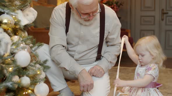 Little Girl Taking Christmas Garland from Box with Help of Granddad alt