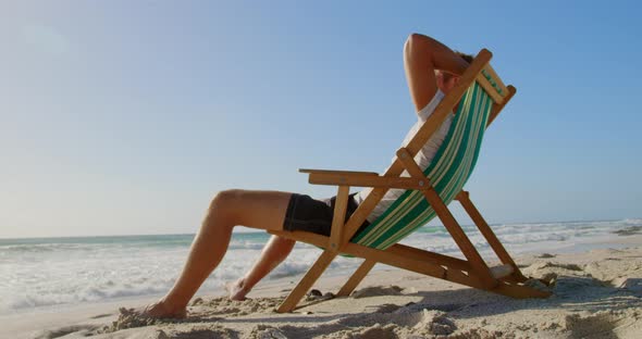 Man with hands behind head relaxing on sun lounger at beach 4k