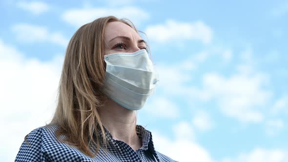 A Girl in a Mask Against the Sky and Clouds Straightens Her Hair. Protection Against the Covid-19 alt