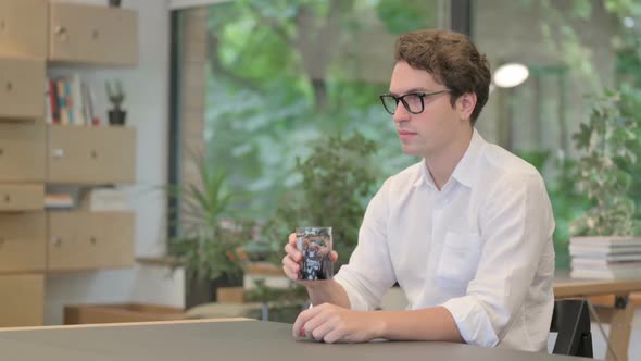 Young Man Drinking Water While Sitting in Office alt
