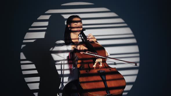 Woman in Spotlight in Studio Plays on Violoncello