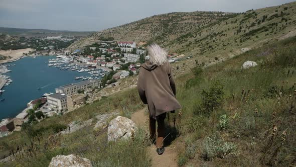 A Man in a Brown Robe with White Hair Descends From the Mountain. From the Back alt