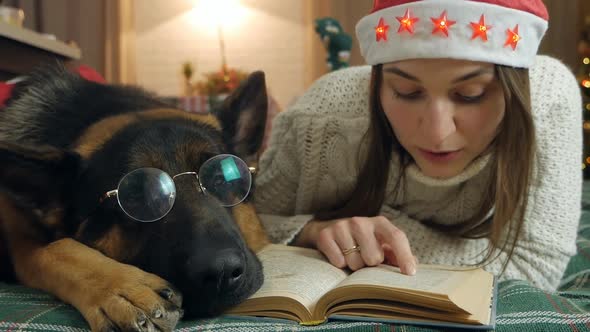 Young Woman and Dog in Glasses are Resting on the Bed at Home