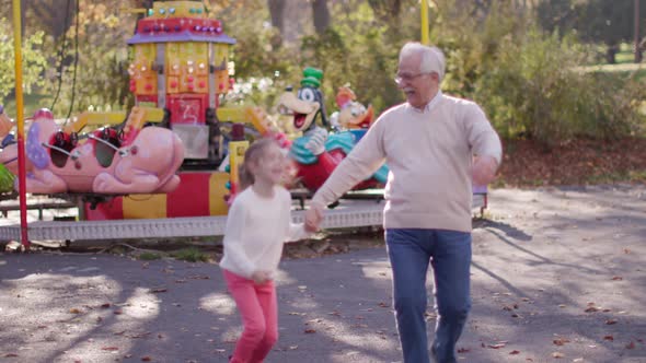 Grandfather having fun with his cute little granddaughter in the amusement park