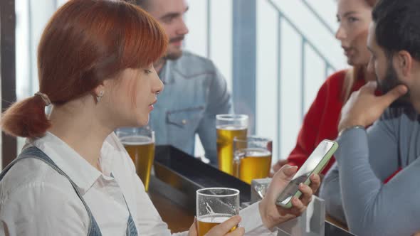 Young Woman Using Her Smart Phone While Drinking Beer at the Pub