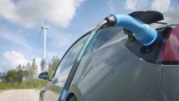 ZOOM IN, GRAPHICS ENHANCED - A generic electric car charges in front of a wind turbine alt