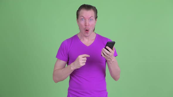 Happy Young Handsome Man Using Phone and Looking Surprised alt