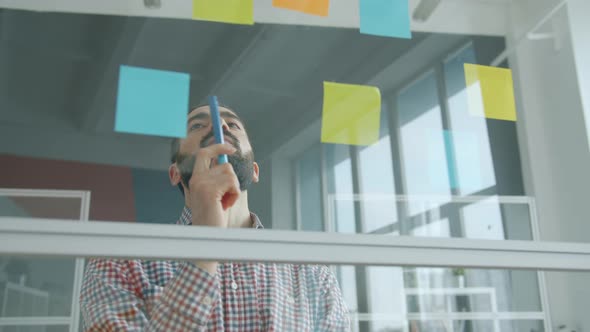 Portrait of Middle Eastern Man Sticking Sticky Notes on Glass Wall in Office alt