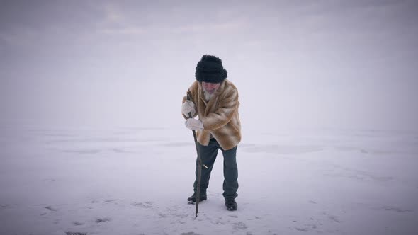 Wide Shot Bearded Senior Man Hitting Stick on Ice in Slow Motion Standing on Frozen Ocean alt