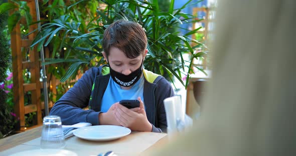 Young Guy in Black Designed Face Mask Types on Smartphone alt