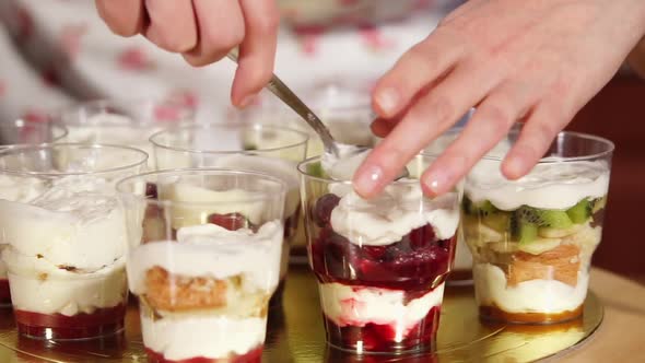 Housewife Is Putting Whipped Cream in a Glass with Red Fruits Jam in Kitchen alt