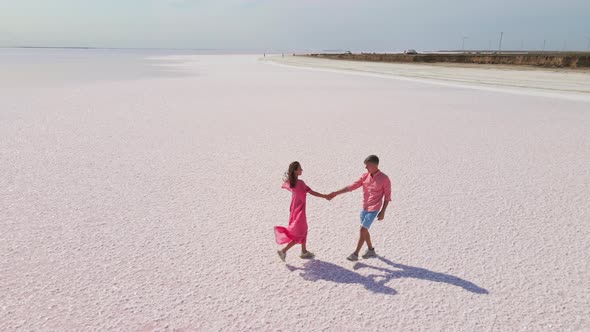 Aerial Drone Footage of Happy Young Couple in Pink Wear Having Fun and Joyfully Running alt
