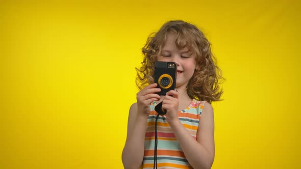 Girl is Using Retro Photo Camera for Shooting Pictures in the Yellow Background alt
