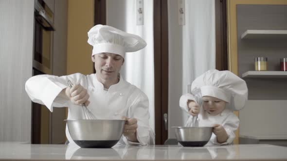 Dad and Son Mixing Food Ingredients in Steel Bowl in Their Home Kitchen alt