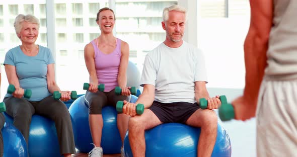 Exercise class sitting on exercise balls lifting hand weights alt