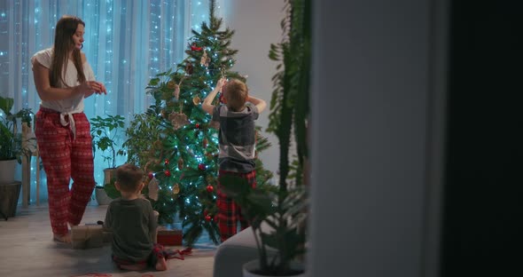 A Family Mother and Two Children Decorate a Christmas Tree with Toys in the Living Room of Their alt