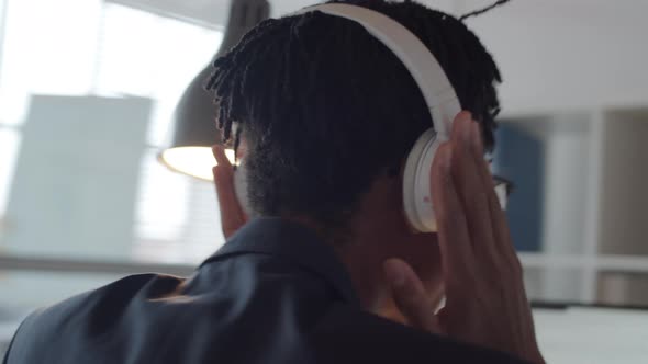 Black Male Office Worker Smiling while Listening to Music with Headphones alt