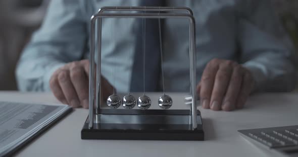 Corporate businessman sitting at desk and playing with Newton's cradle balance balls