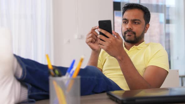 Indian Man with Smartphone Resting Feet on Table alt